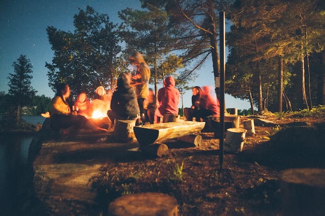 People sitting outside on benches around a fire