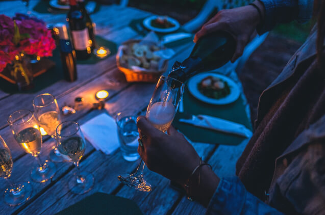 A person pouring champagne into a glass at a backyard dinner party with a tent.
