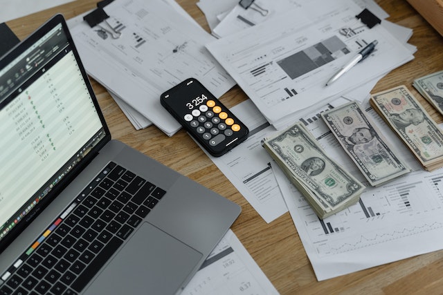 A laptop, calculator, and divided piles of money for budget management in event planning.